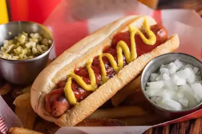 hot dog covered in mustard and ketchup next to relish and onions