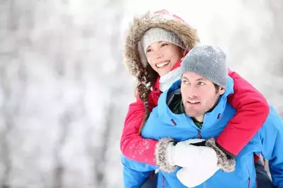 A man giving his girlfriend a piggyback ride during a winter hike in the forest.