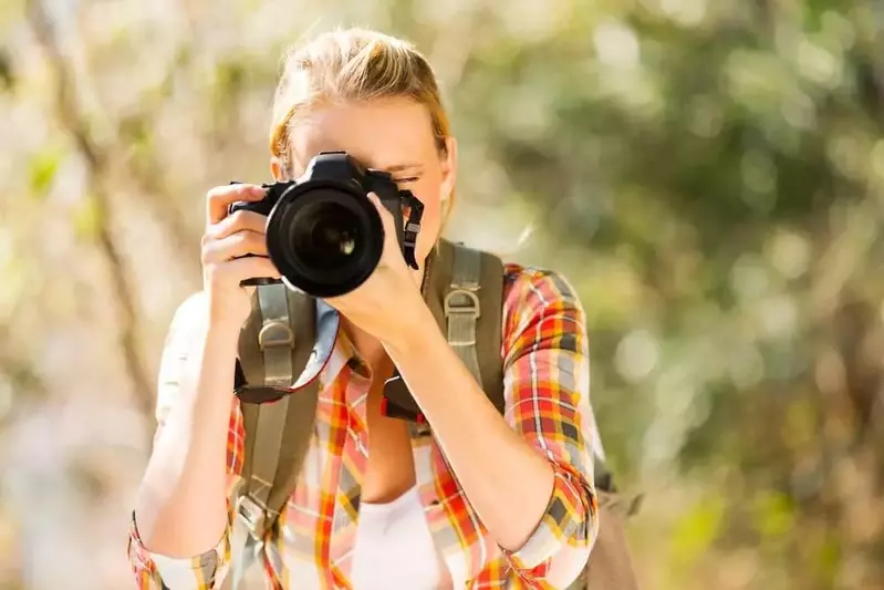 A woman taking a photo in the woods.