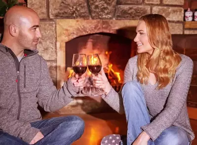 A man and a woman with glasses of wine in front of the fireplace at one of our most romantic Gatlinburg cabin rentals for couples.