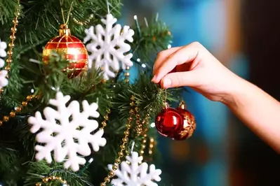 A woman's hand decorating a Christmas tree with ornaments.