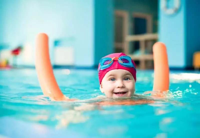 Happy little girl swimming with a noodle in indoor pool