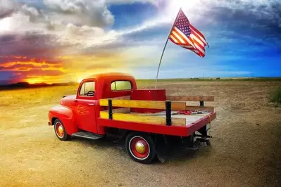 Red pickup truck facing a cloudy sky with the American flag in the back